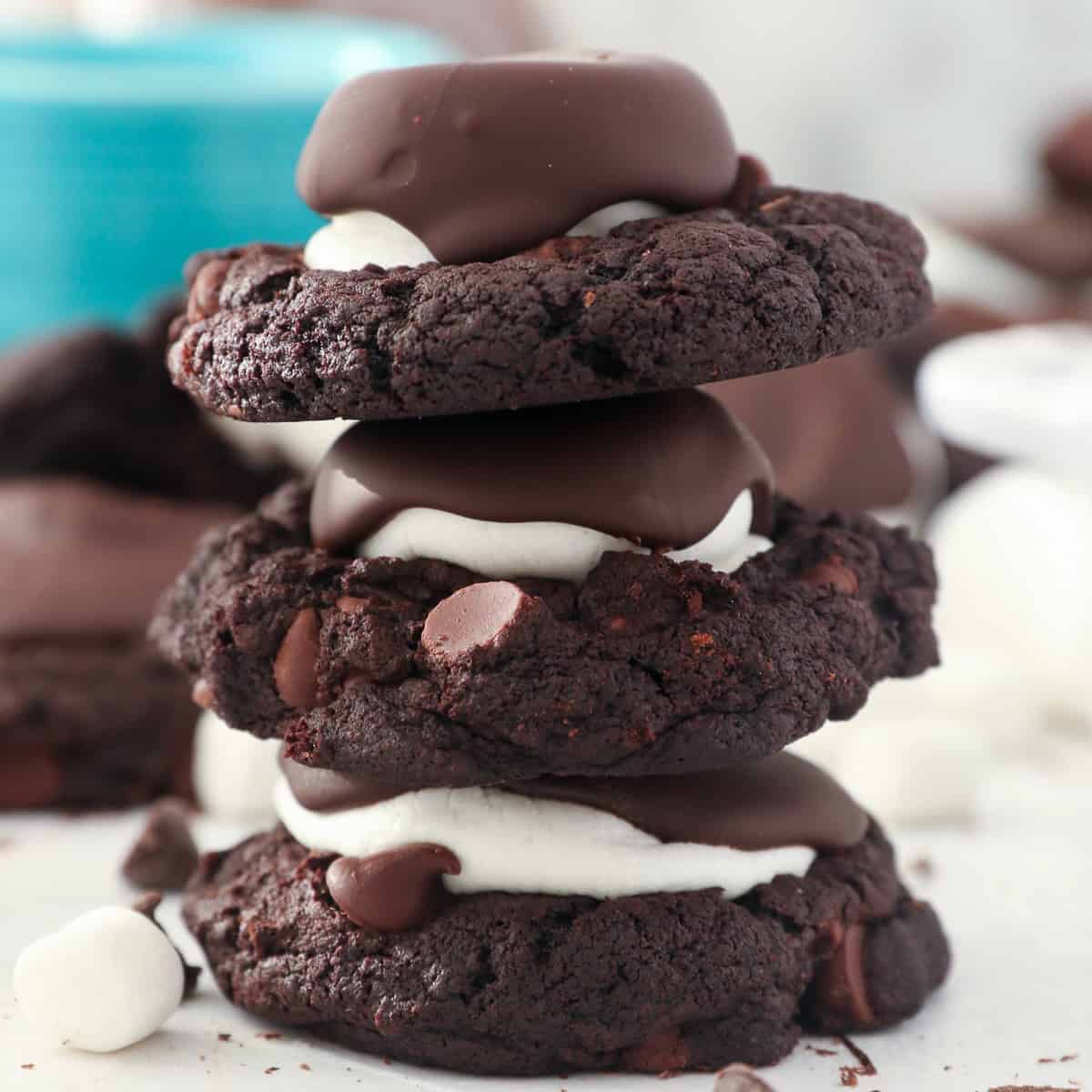 A stack of 3 hot chocolate cookies with a marshmallow in the middle and covered in chocolate
