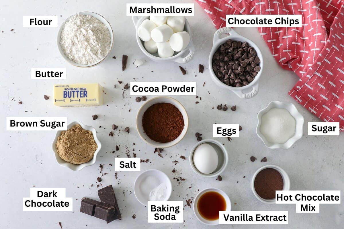 Ingredients for hot chocolate cookies laid out in in white bowls with a pink napkin