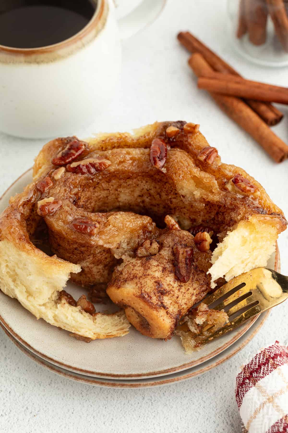These homemade sticky buns are filled with warm cinnamon and nutty pecans, with a gooey caramel topping. The dough needs just 1 hour to rise! A homemade sticky bun with a forkful missing on a plate.