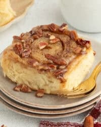 A sticky bun topped with caramel and pecans on a plate.