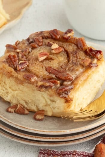 A sticky bun topped with caramel and pecans on a plate.