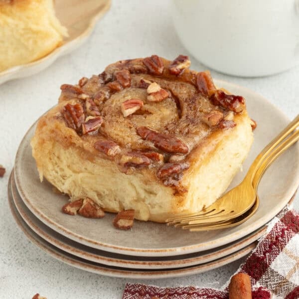 A sticky bun topped with caramel and pecans on a plate.