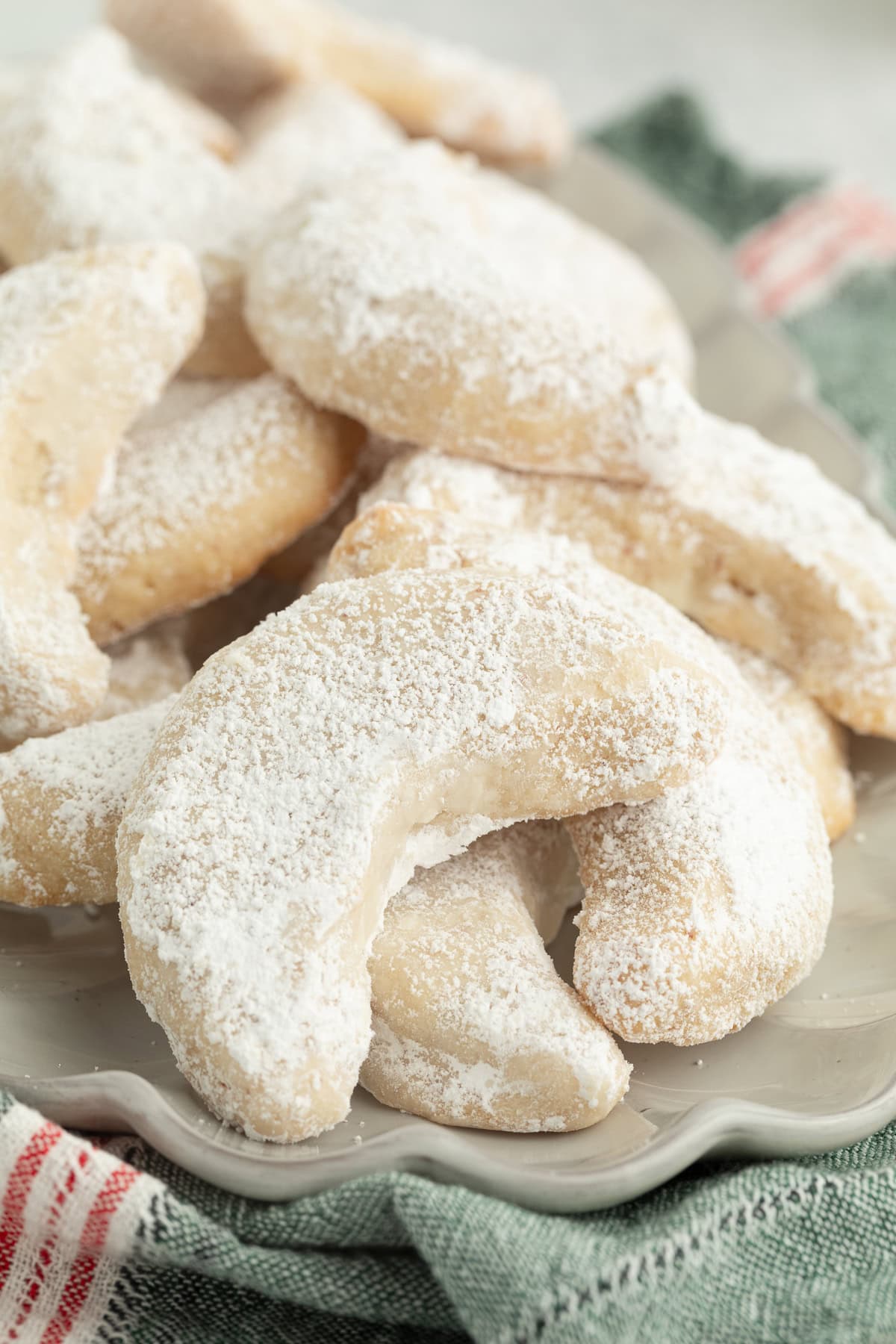 These classic almond crescent cookies have a buttery, crumbly shortbread texture and a sweet powdered sugar coating. No chilling needed! Close up of almond crescent cookies piled on a plate.