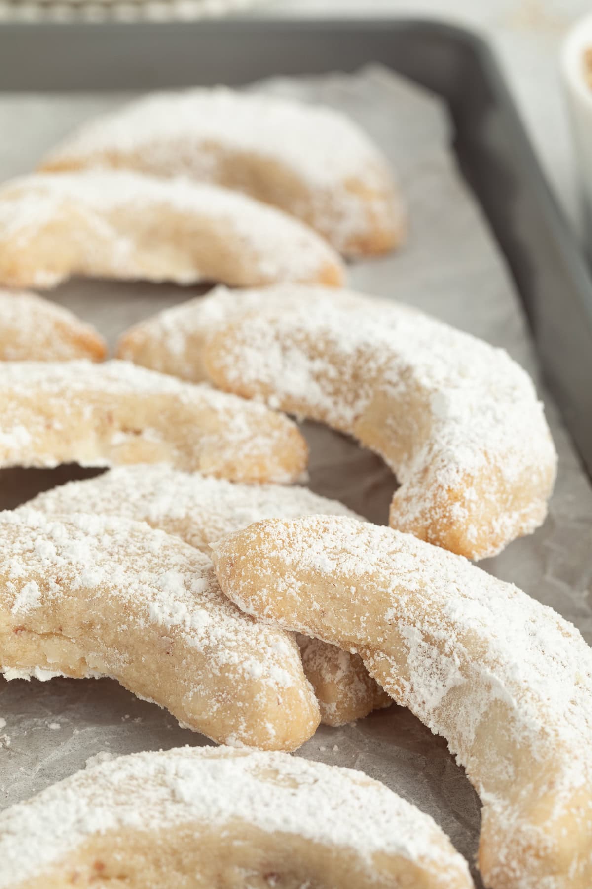 These classic almond crescent cookies have a buttery, crumbly shortbread texture and a sweet powdered sugar coating. No chilling needed! Assorted almond crescent cookies dusted with powdered sugar on a parchment-lined baking sheet.