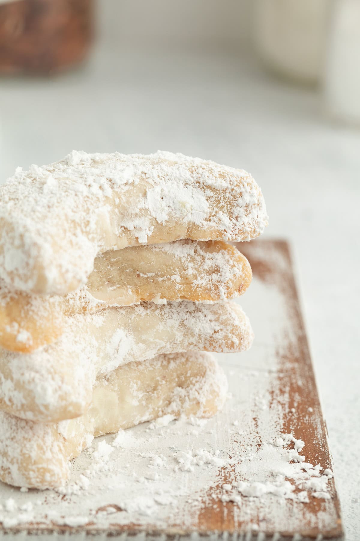 These classic almond crescent cookies have a buttery, crumbly shortbread texture and a sweet powdered sugar coating. No chilling needed! Four almond crescent cookies dusted with powdered sugar stacked on a wooden cutting board.