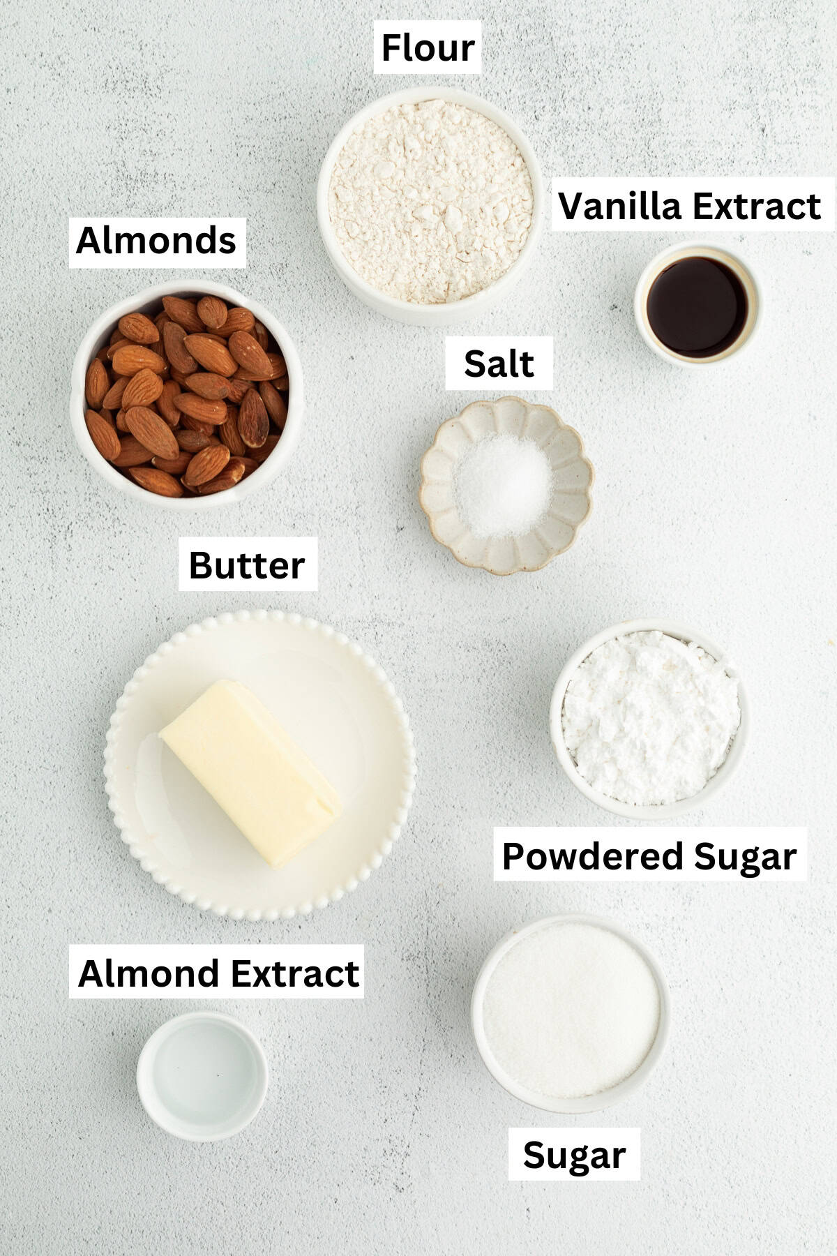 These classic almond crescent cookies have a buttery, crumbly shortbread texture and a sweet powdered sugar coating. No chilling needed! Almond crescent cookies ingredients with text labels overlaying each ingredient.