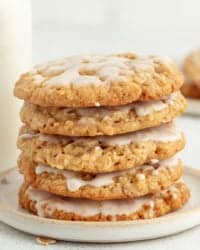 Iced oatmeal cookies stacked on a stoneware plate with a jug of milk in the background.