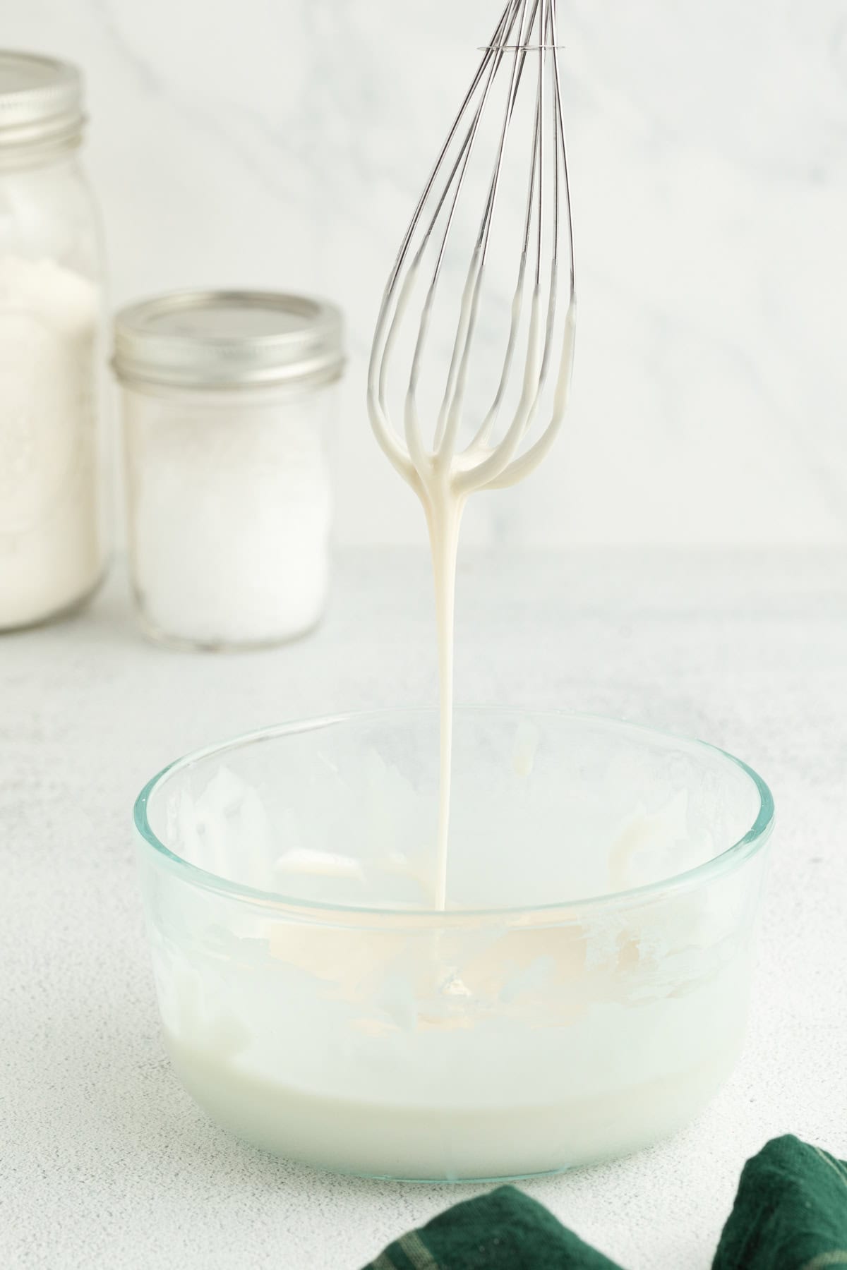 These old-fashioned iced oatmeal cookies have soft middles, crispy edges, and plenty of brown sugar and cinnamon, topped with vanilla icing. A whisk dripping with icing held over more icing in a mixing bowl.