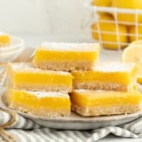 A stack of five lemon bars dusted with powdered sugar on a plate.