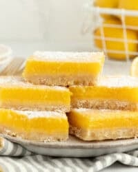 A stack of five lemon bars dusted with powdered sugar on a plate.