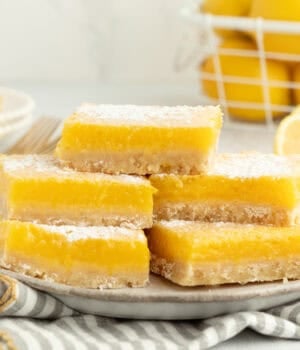 A stack of five lemon bars dusted with powdered sugar on a plate.