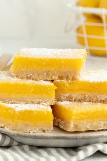 A stack of five lemon bars dusted with powdered sugar on a plate.