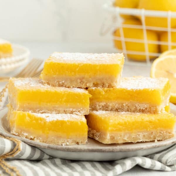 A stack of five lemon bars dusted with powdered sugar on a plate.