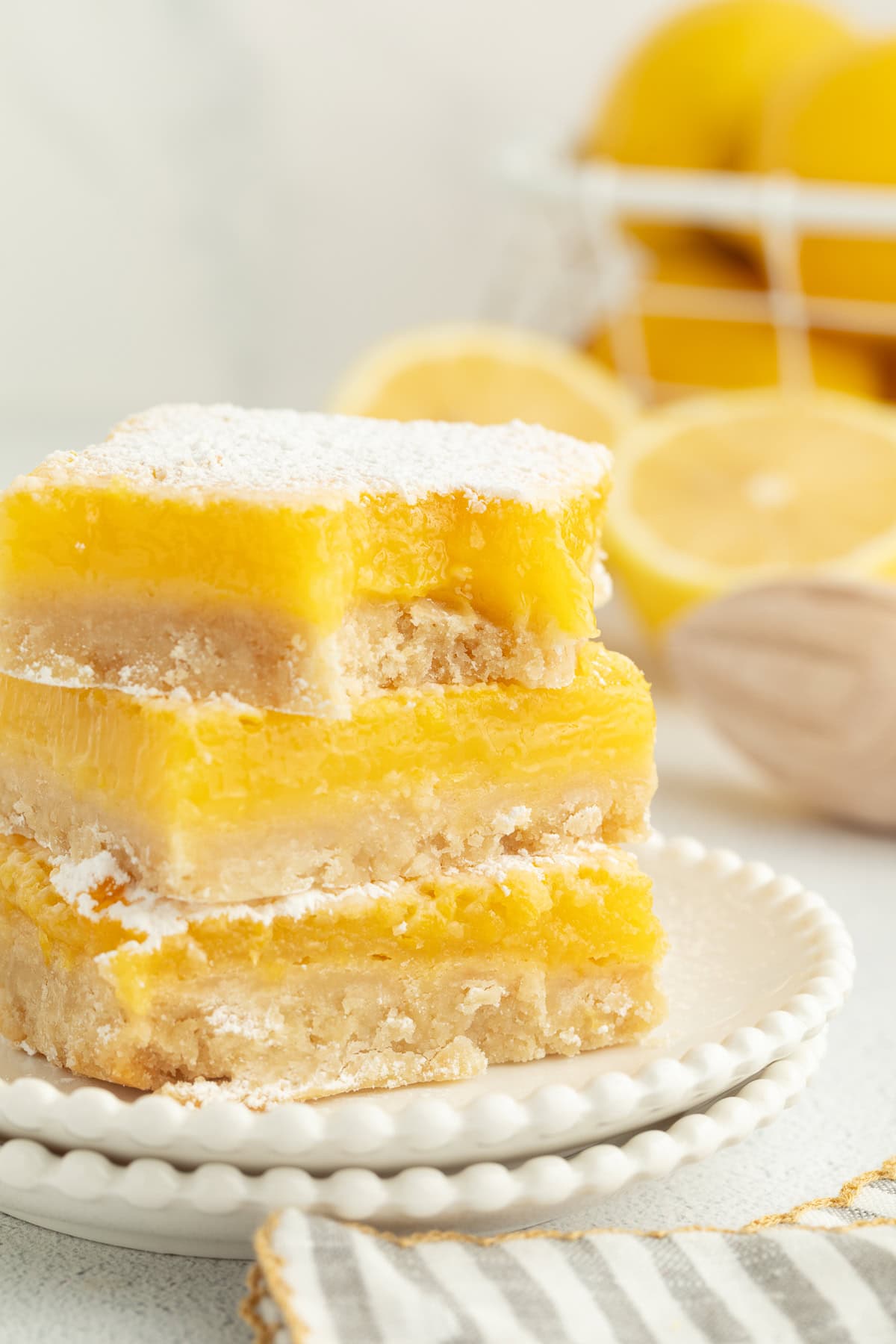 Make the best lemon bars that are perfectly baked with a soft, buttery shortbread crust and a sweet, tangy, creamy lemon curd filling. A stack of three lemon bars dusted with powdered sugar on a plate, with a bite missing from the top bar.