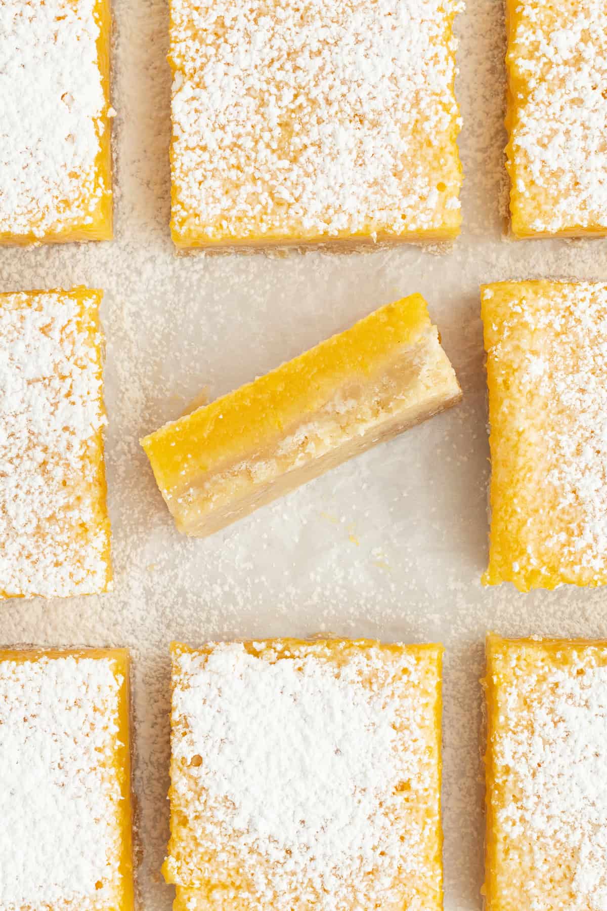 Make the best lemon bars that are perfectly baked with a soft, buttery shortbread crust and a sweet, tangy, creamy lemon curd filling. Overhead view of assorted lemon bars dusted with powdered sugar, with one bar turned on its side to show the thick lemon layer.
