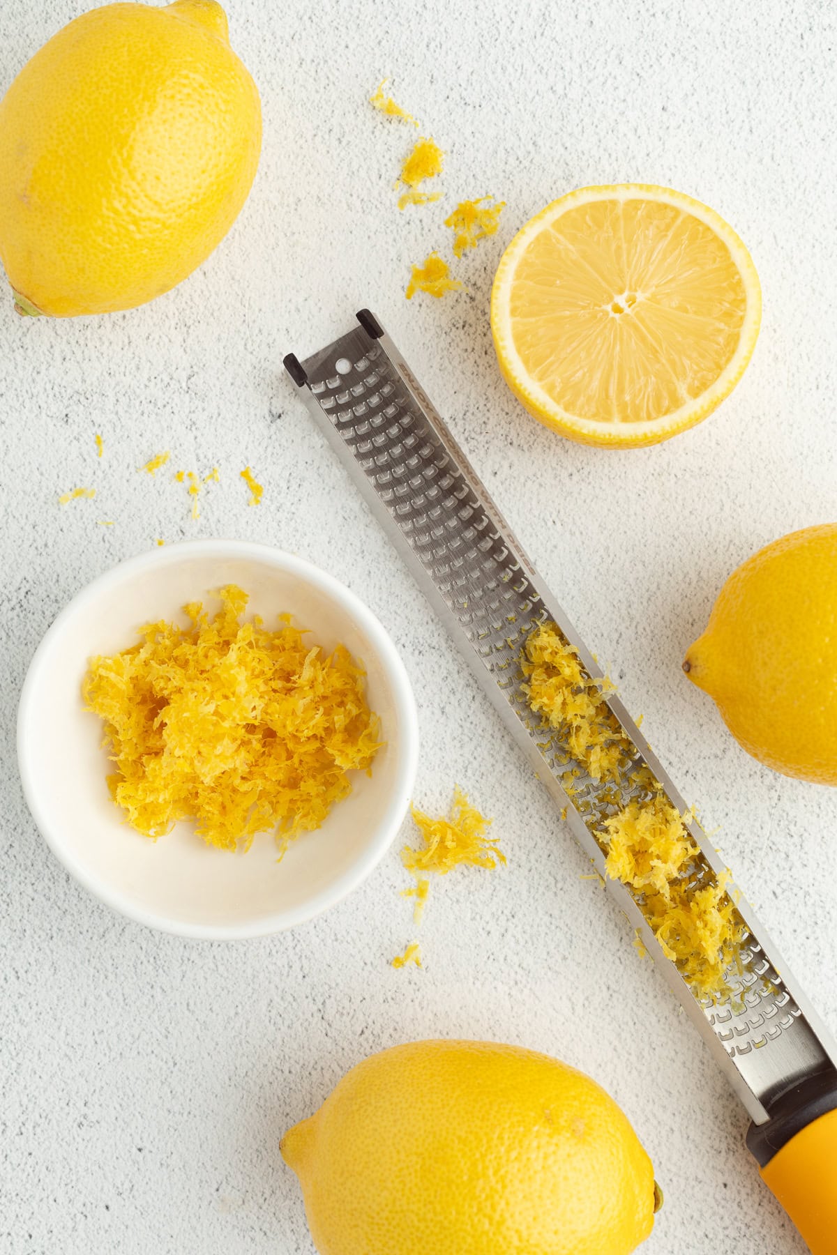 Make the best lemon bars that are perfectly baked with a soft, buttery shortbread crust and a sweet, tangy, creamy lemon curd filling. Overhead view of a microplane with lemon zest next to whole lemons and a bowl of lemon zest.