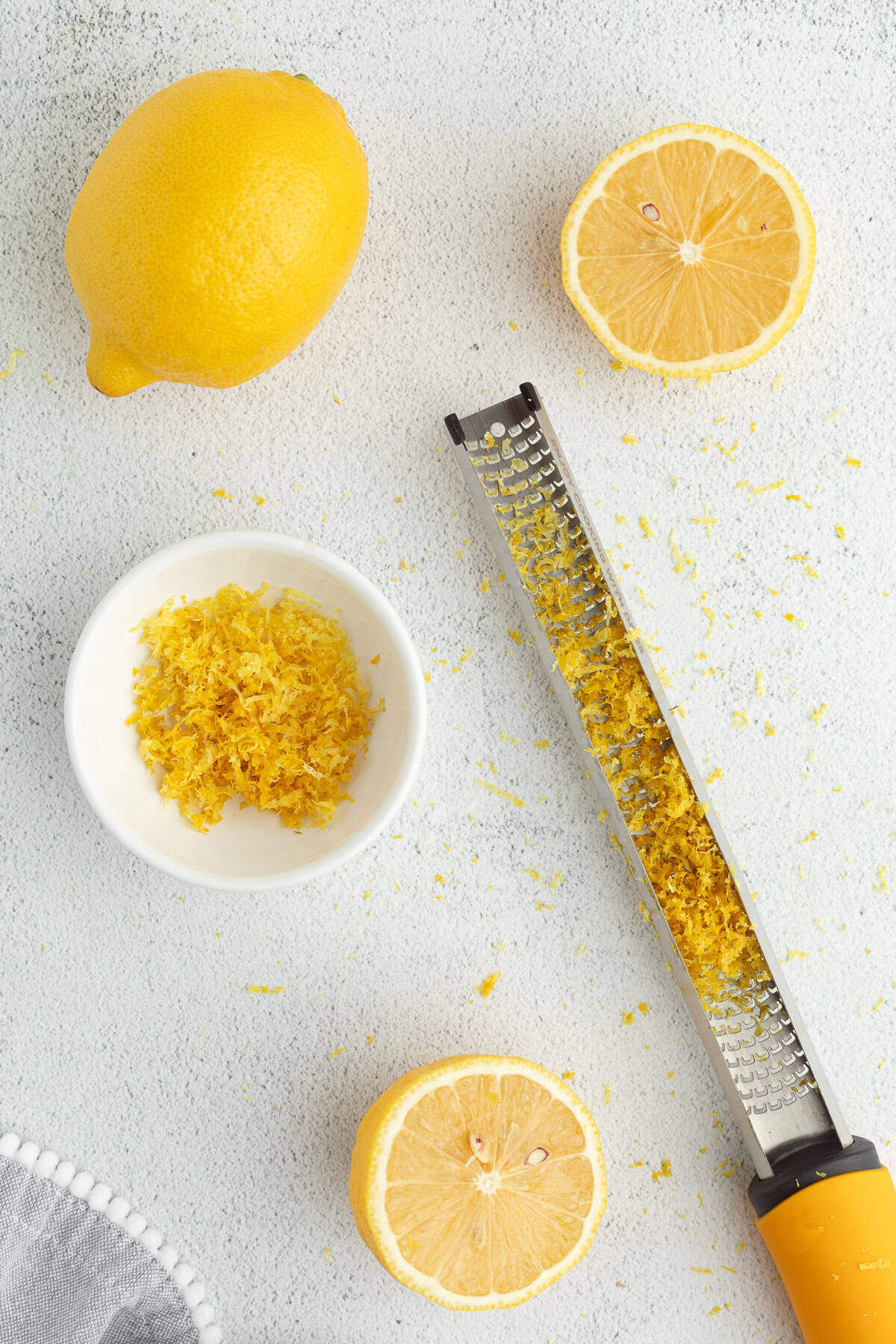 Moist, tangy, and topped with sanding sugar, these bakery-style lemon poppyseed muffins are the perfect breakfast treat. And so easy to make! Overhead view of a mircoplane with lemon zest next to a small bowl with more zest and whole and half lemons.