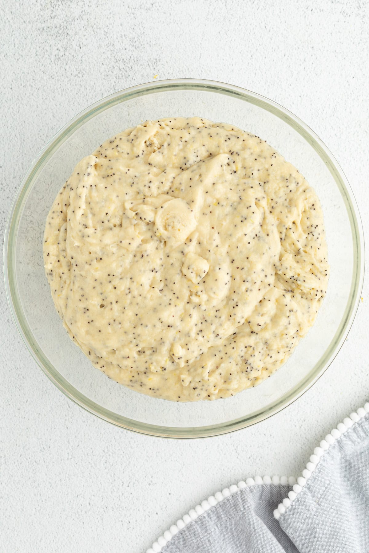 Moist, tangy, and topped with sanding sugar, these bakery-style lemon poppyseed muffins are the perfect breakfast treat. And so easy to make! Lemon poppy seed muffin batter in a glass bowl.