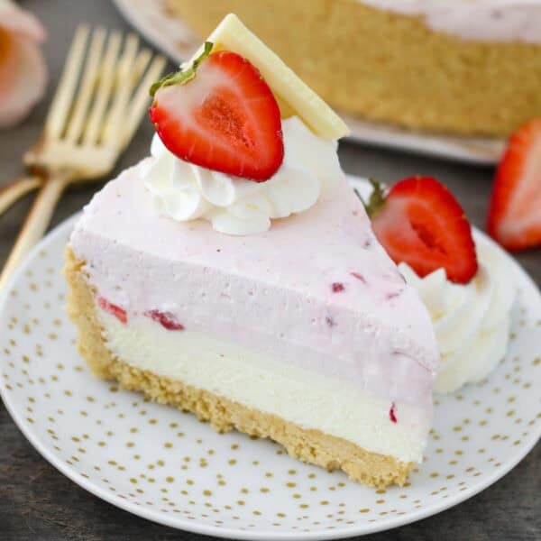 A slice of strawberry mousse cake decorated with whipped cream and a fresh strawberry.