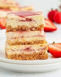 Three strawberry cheesecake bars stacked on a plate.