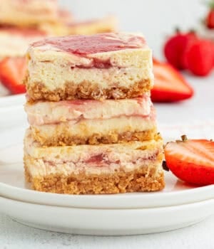 Three strawberry cheesecake bars stacked on a plate.