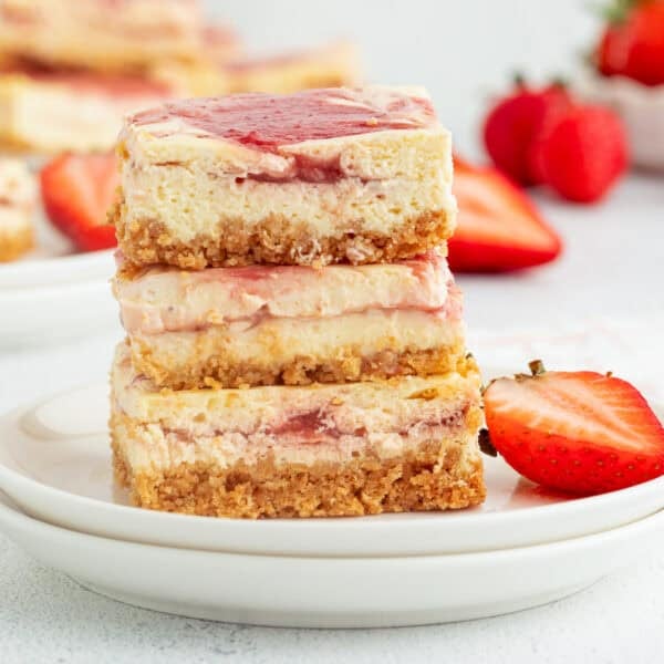 Three strawberry cheesecake bars stacked on a plate.