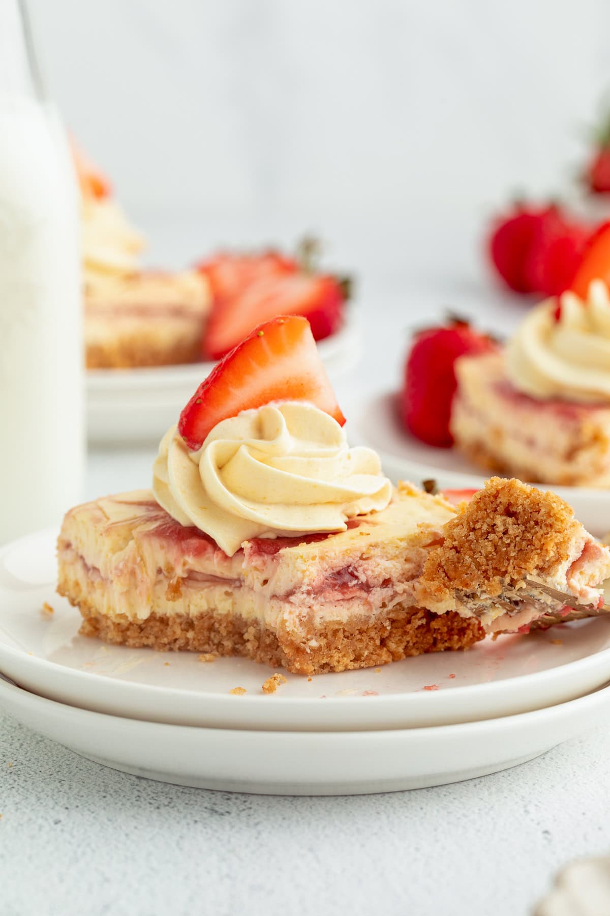 Strawberry cheesecake bars are easier to bake than a classic cheesecake, with a buttery crust and rich filling swirled with strawberry sauce! A strawberry cheesecake bar topped with a swirl of whipped cream and a fresh strawberry with a forkful missing.