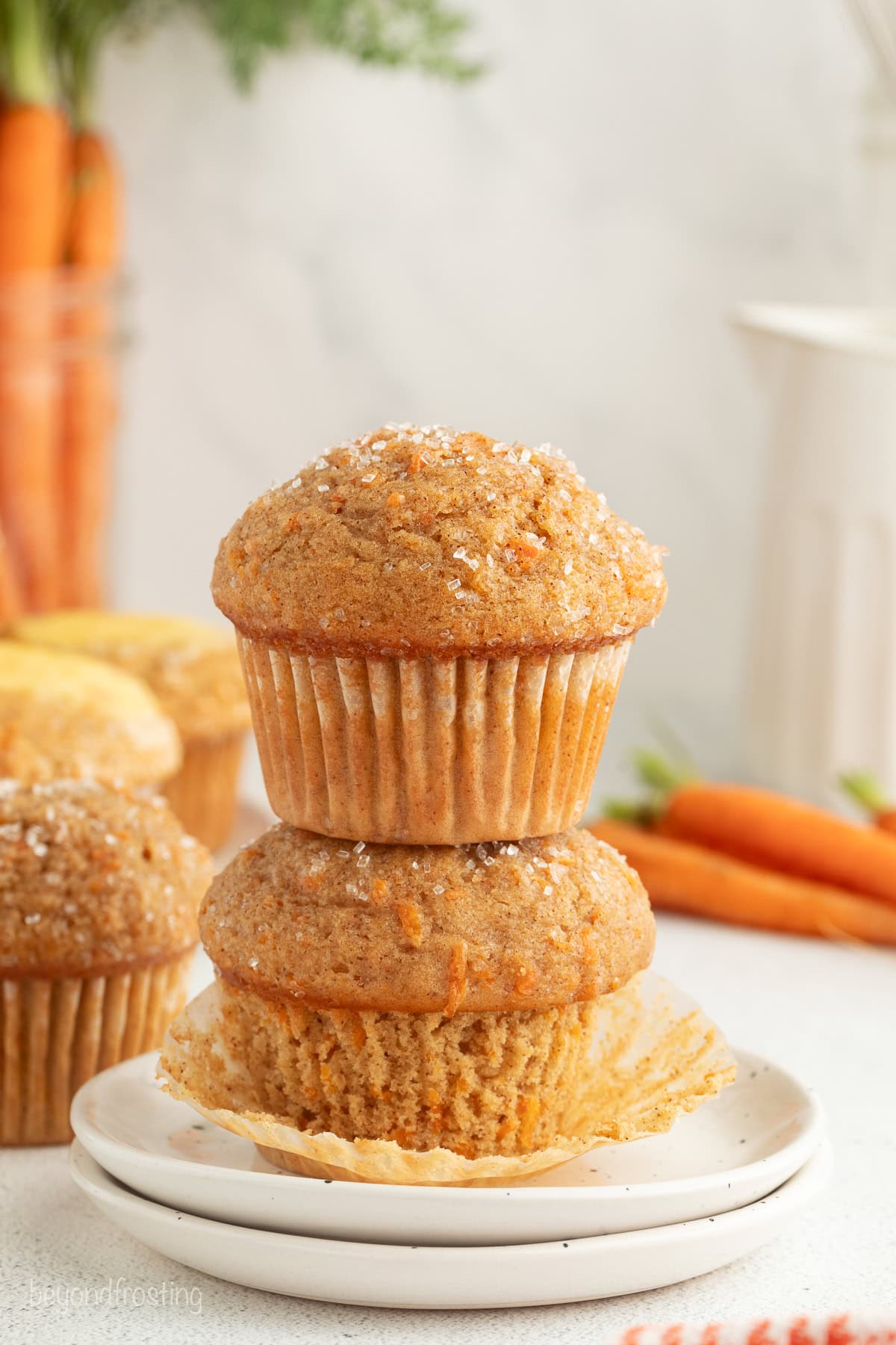 Sweet, moist carrot cake muffins are full of carrot cake flavor! They're easy to make, with the option to add a sweet cream cheese filling. Two carrot cake muffins stacked on a plate.