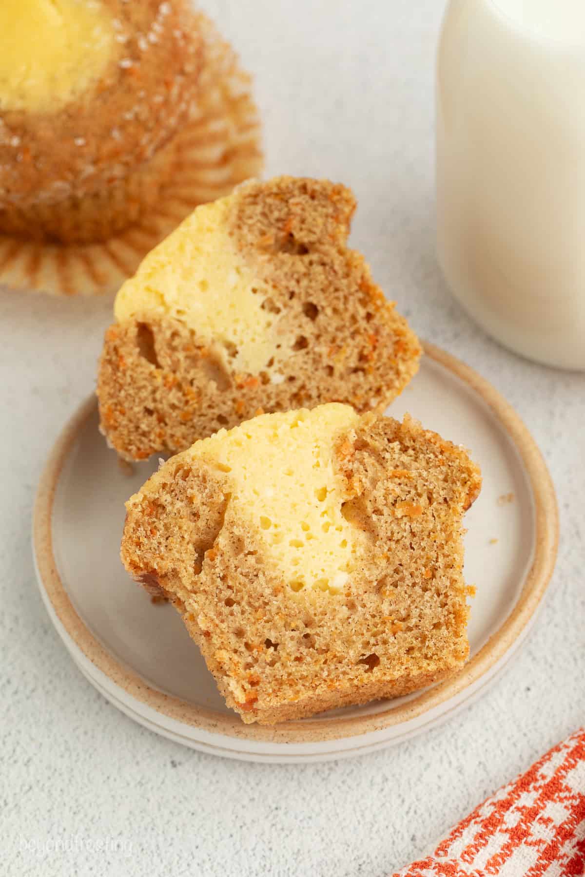 Sweet, moist carrot cake muffins are full of carrot cake flavor! They're easy to make, with the option to add a sweet cream cheese filling. Close up of a carrot cake muffin sliced in half to show the cream cheese filling.