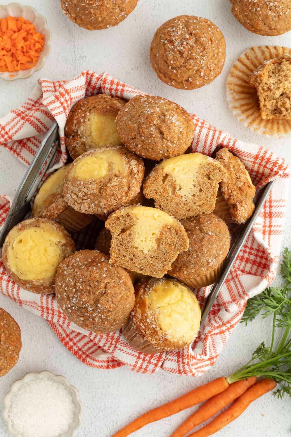 Sweet, moist carrot cake muffins are full of carrot cake flavor! They're easy to make, with the option to add a sweet cream cheese filling. Overhead view of assorted carrot cake muffins piled in a basket, some sliced in half to show the cream cheese filling.