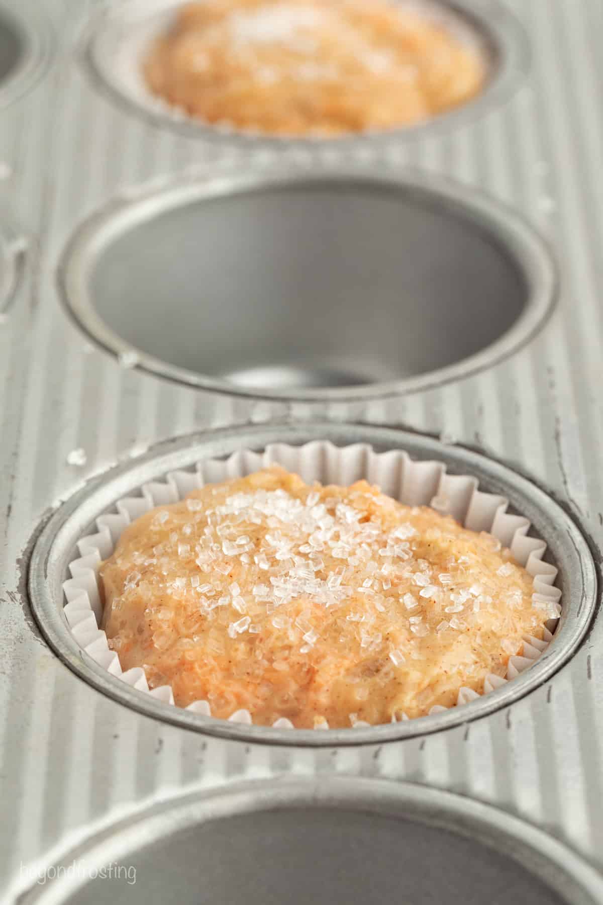 Sweet, moist carrot cake muffins are full of carrot cake flavor! They're easy to make, with the option to add a sweet cream cheese filling. Carrot muffin batter topped with sanding sugar in a muffin well.