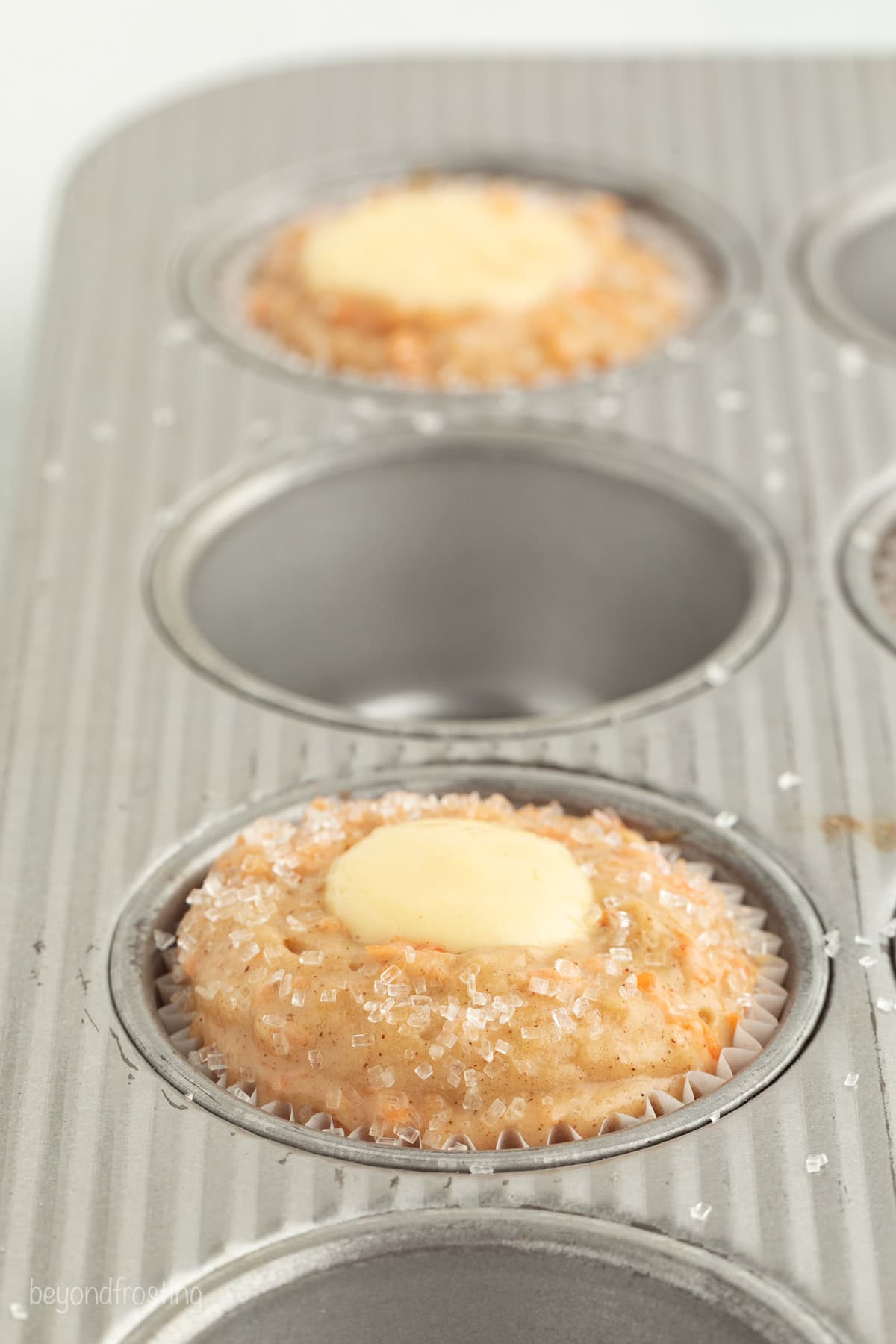 Sweet, moist carrot cake muffins are full of carrot cake flavor! They're easy to make, with the option to add a sweet cream cheese filling. A muffin pan where every other well is filled with carrot muffin batter with cream cheese centers.