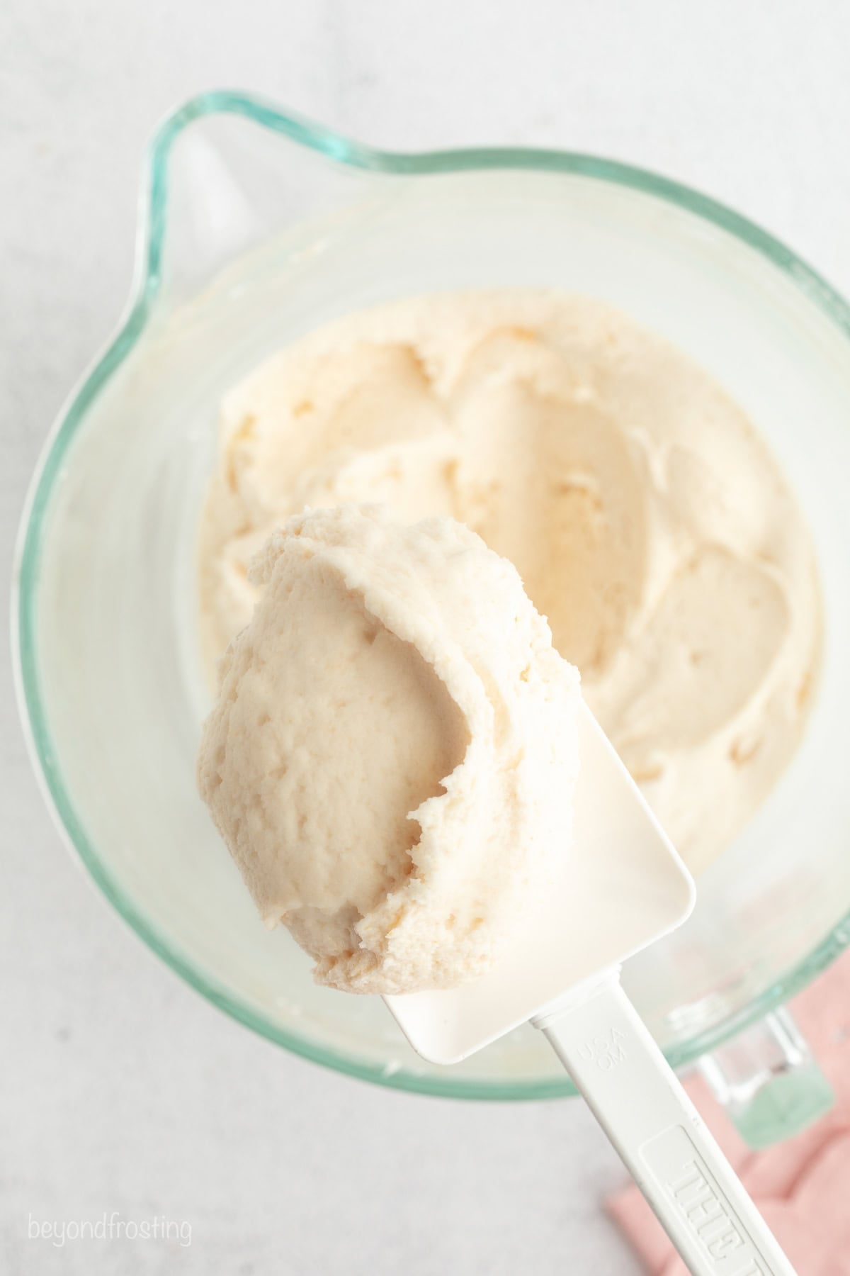 Hummingbird cake is a soft, spiced Southern layer cake with sweet banana, crushed pineapple, crunchy pecans, and cream cheese frosting. Close up of brown butter cream cheese frosting on a spatula held over a bowl.