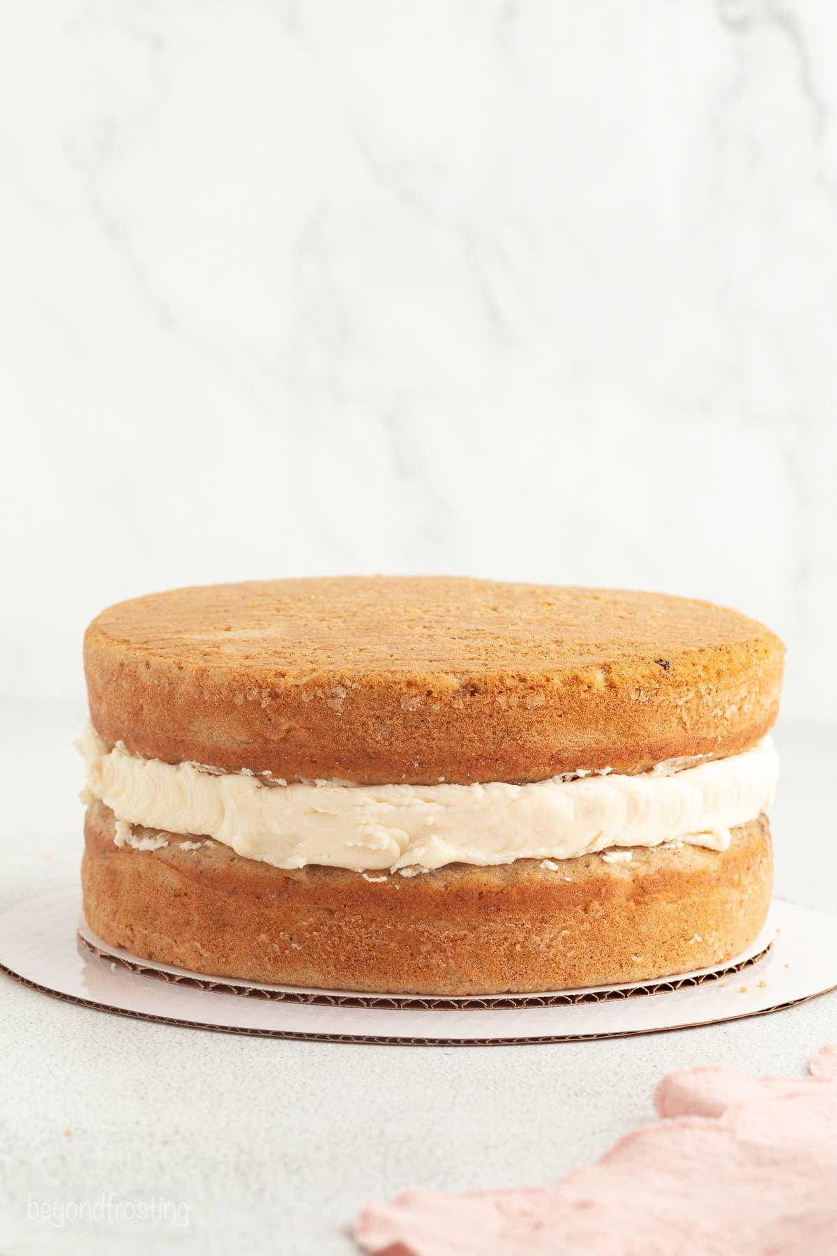 Hummingbird cake is a soft, spiced Southern layer cake with sweet banana, crushed pineapple, crunchy pecans, and cream cheese frosting. Two hummingbird cake layers filled with cream cheese frosting on a cake board.