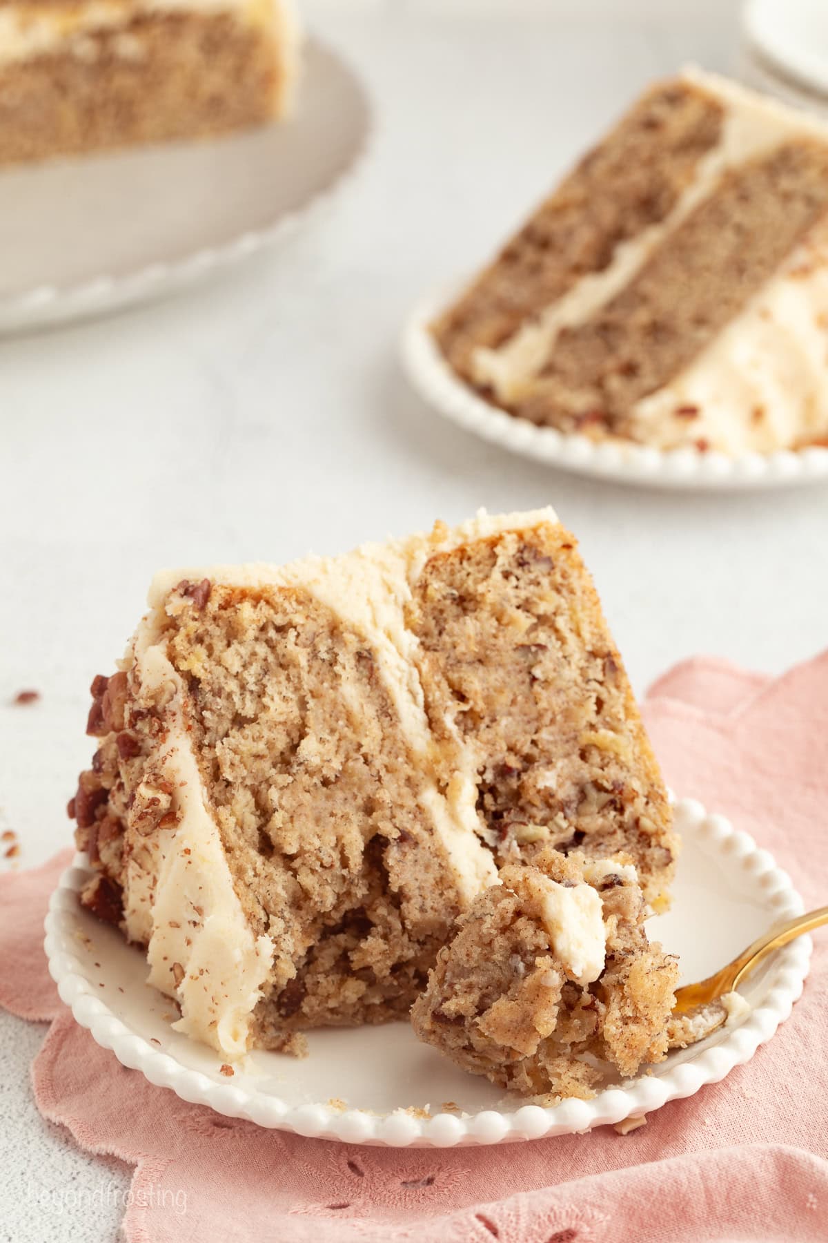 Hummingbird cake is a soft, spiced Southern layer cake with sweet banana, crushed pineapple, crunchy pecans, and cream cheese frosting. A slice of hummingbird cake next to a forkful on a plate.