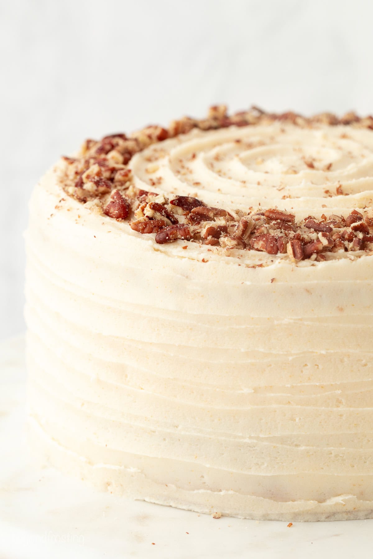 Hummingbird cake is a soft, spiced Southern layer cake with sweet banana, crushed pineapple, crunchy pecans, and cream cheese frosting. Close up of a whole frosted hummingbird cake on a cake stand.
