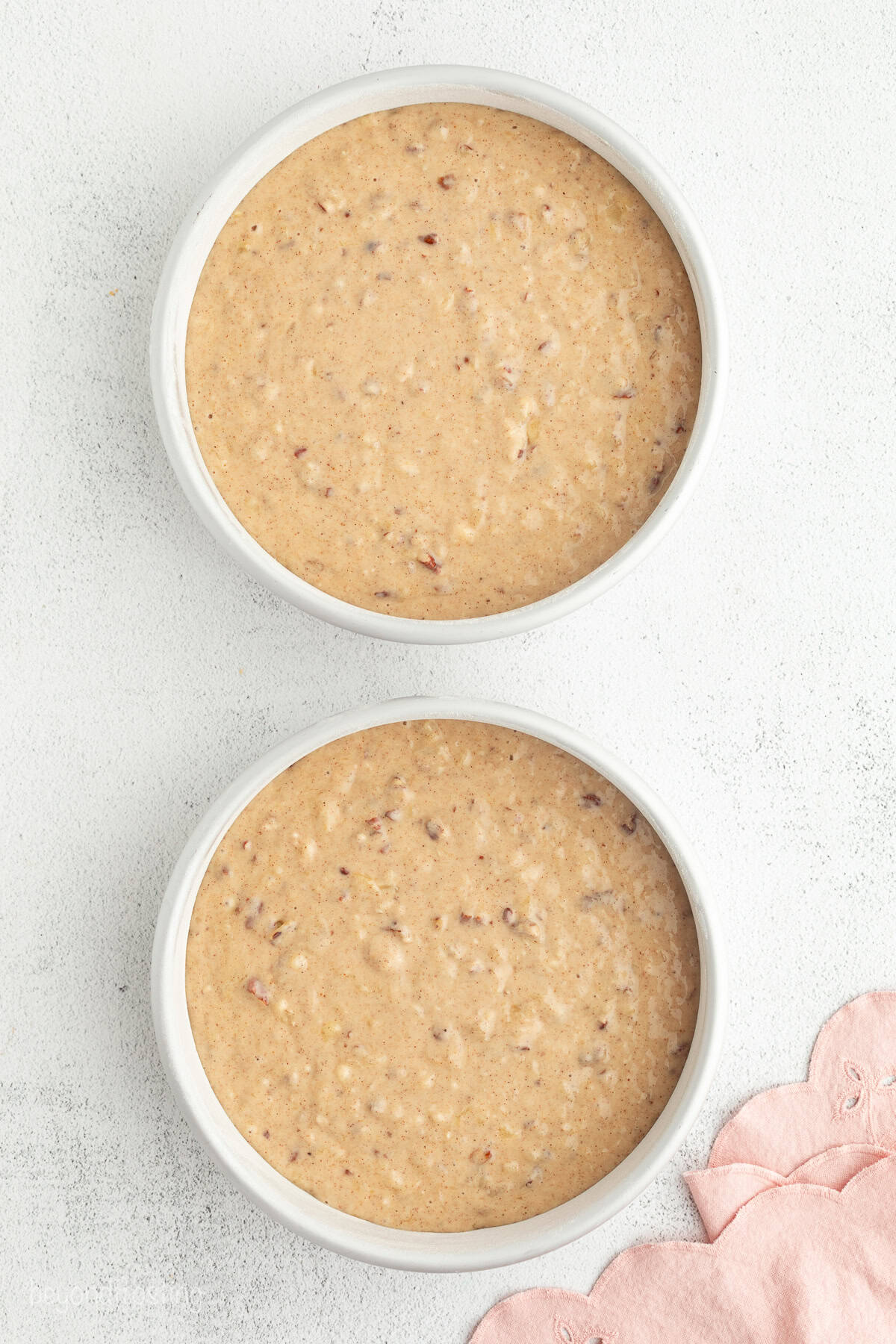 Hummingbird cake is a soft, spiced Southern layer cake with sweet banana, crushed pineapple, crunchy pecans, and cream cheese frosting. Overhead view of two cake pans filled with hummingbird cake batter.