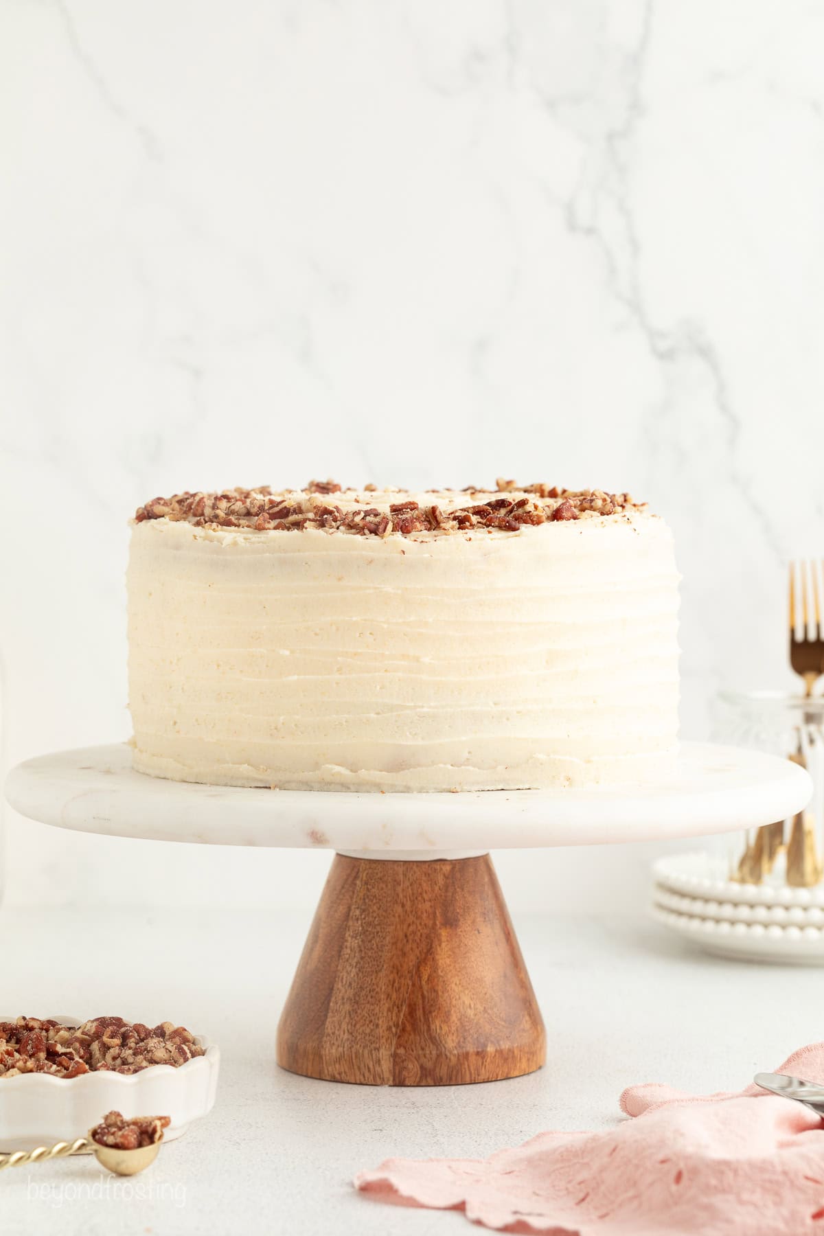 Hummingbird cake is a soft, spiced Southern layer cake with sweet banana, crushed pineapple, crunchy pecans, and cream cheese frosting. A whole frosted hummingbird cake on a cake stand.