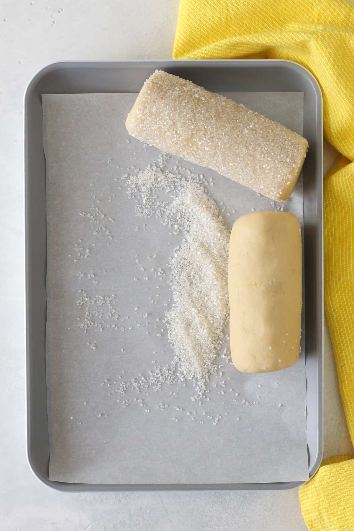 These slice-and-bake lemon shortbread cookies are crisp, buttery, and melt-in-your-mouth, rolled in sanding sugar for sweet, crunchy edges. Overhead view of logs of lemon shortbread cookie dough rolled in sugar.