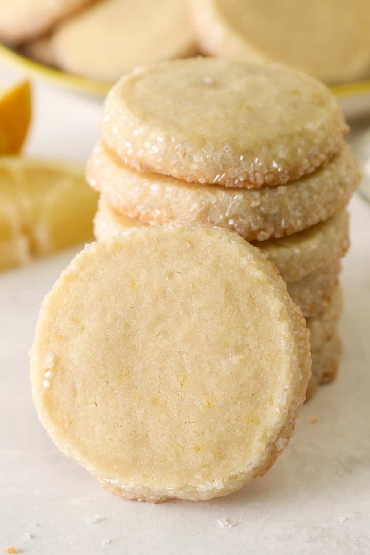 These slice-and-bake lemon shortbread cookies are crisp, buttery, and melt-in-your-mouth, rolled in sanding sugar for sweet, crunchy edges. A lemon shortbread cookie leaning against a stack of cookies.