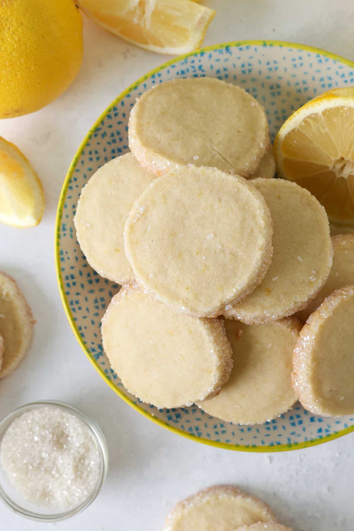 These slice-and-bake lemon shortbread cookies are crisp, buttery, and melt-in-your-mouth, rolled in sanding sugar for sweet, crunchy edges. Overhead view of assorted lemon shortbread cookies piled on a plate.