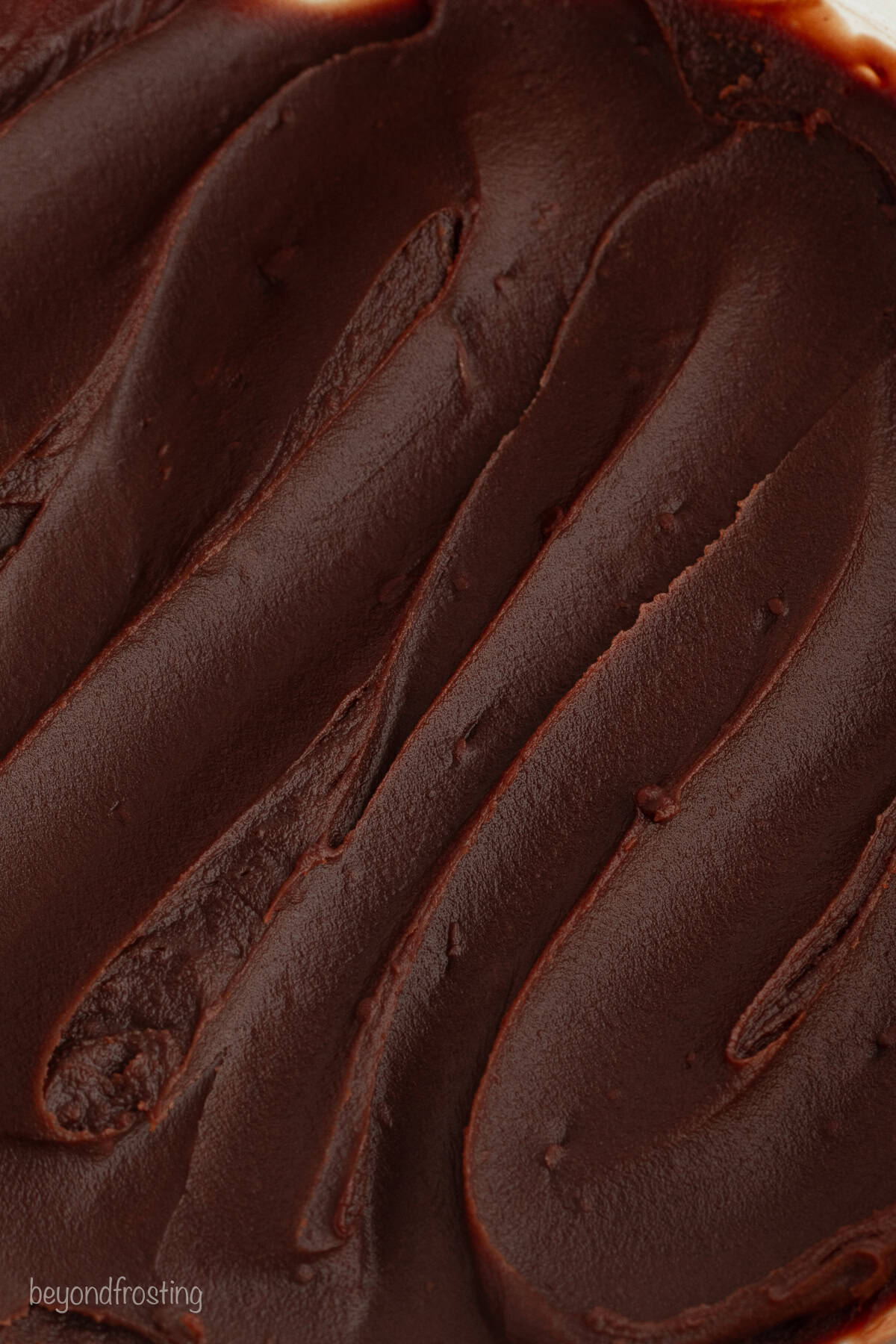 This homemade Boston cream pie is an airy sponge cake filled with pastry cxream and glazed with rich chocolate ganache, all made from scratch! Close up of chocolate ganache.