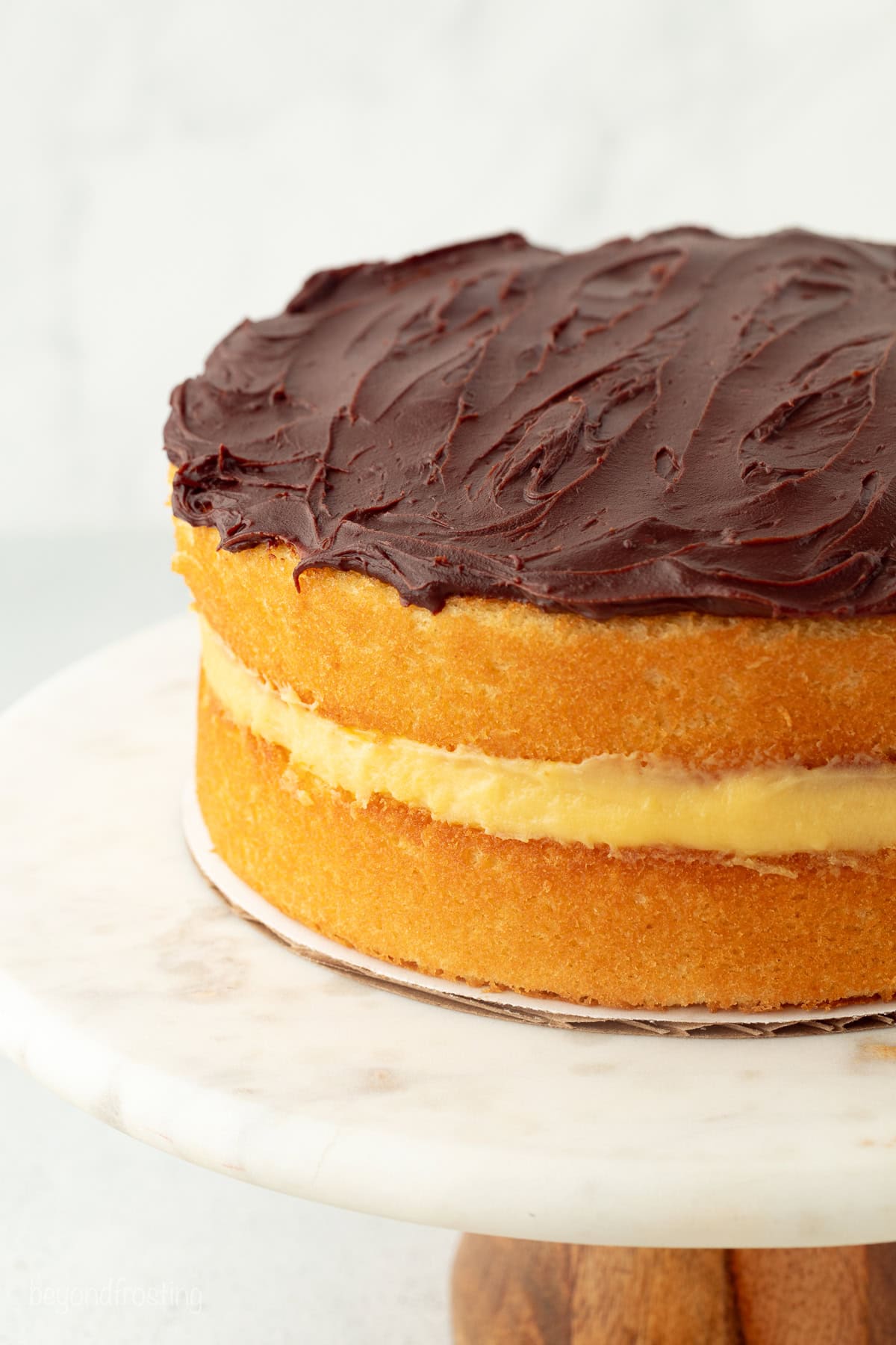 This homemade Boston cream pie is an airy sponge cake filled with pastry cxream and glazed with rich chocolate ganache, all made from scratch! Homemade Boston cream pie with chocolate ganache on a cake stand.