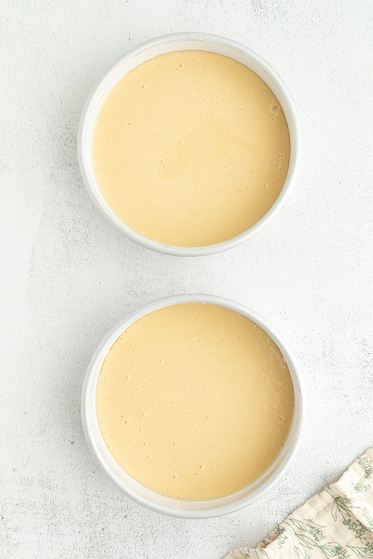 This homemade Boston cream pie is an airy sponge cake filled with pastry cxream and glazed with rich chocolate ganache, all made from scratch! Overhead view of the cake batter for Boston cream pie in two round cake pans.