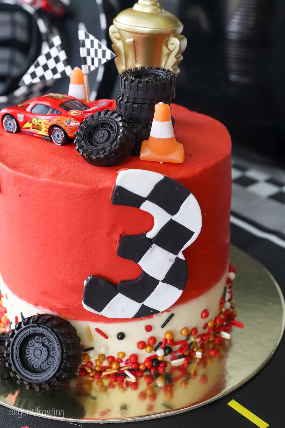With racing-red frosting and just a little fondant, this Lightning McQueen layer cake is perfect for a kids’ Cars birthday party! A Lightning McQueen cake with racing themed decorations, turned to show the fondant number 3.