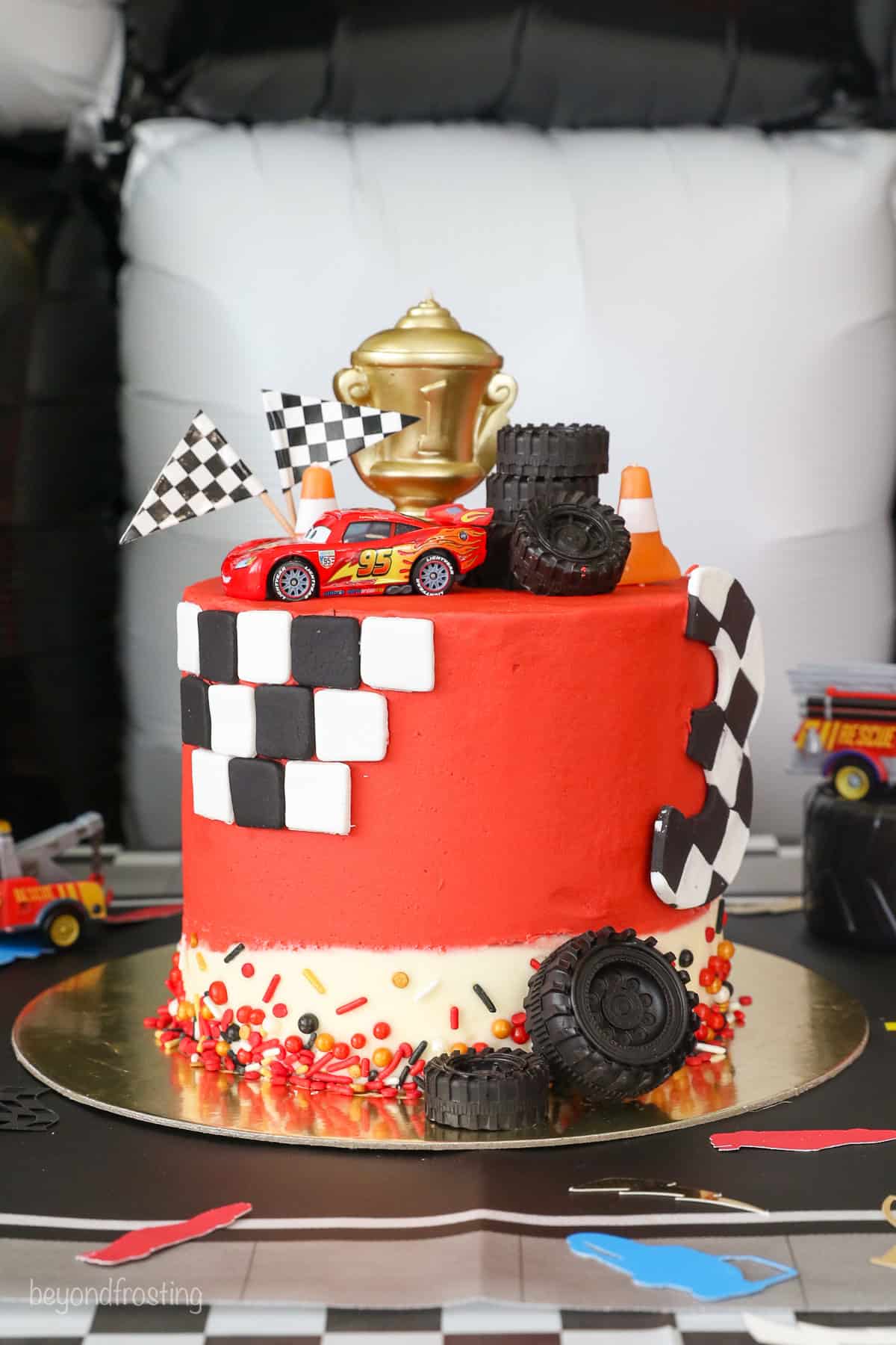 With racing-red frosting and just a little fondant, this Lightning McQueen layer cake is perfect for a kids’ Cars birthday party! A Lightning McQueen cake with racing themed decorations.