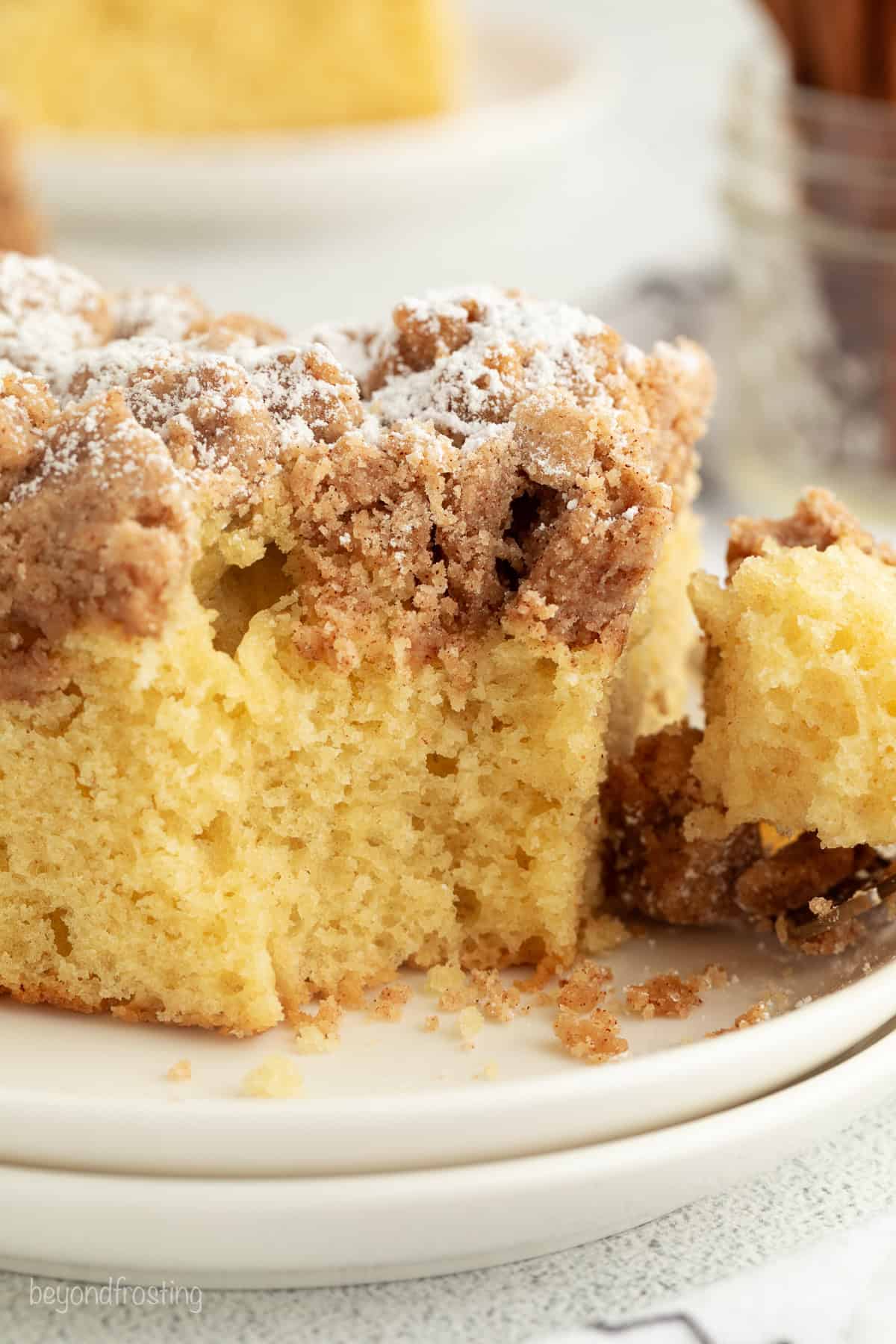 This New York crumb cake is tender and buttery, piled high with a thick brown sugar cinnamon streusel that’s almost as thick as the cake. Close up of a slice of homemade crumb cake with buttery topping, with a forkful missing.