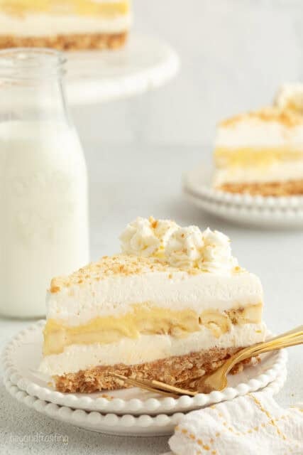 A slice of no-bake banana pudding cheesecake topped with whipped cream and Nilla wafer crumbs on a plate.