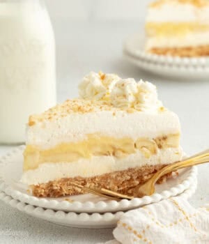 A slice of no-bake banana pudding cheesecake topped with whipped cream and Nilla wafer crumbs on a plate.