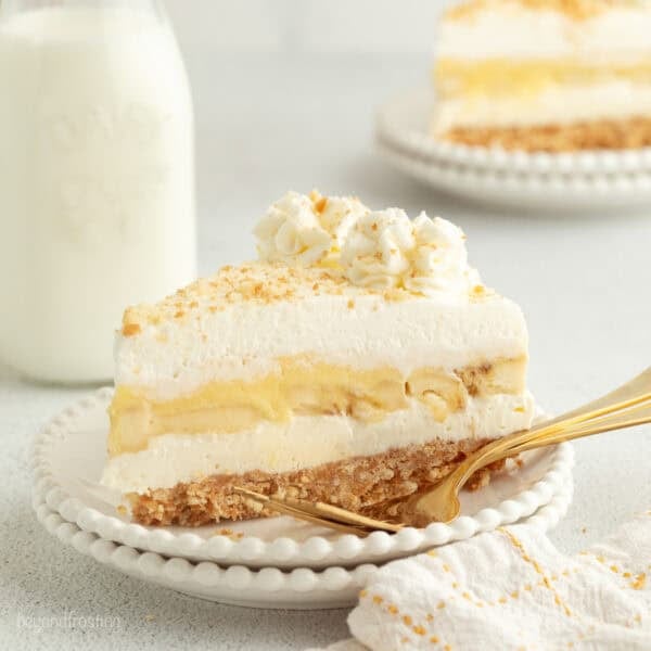 A slice of no-bake banana pudding cheesecake topped with whipped cream and Nilla wafer crumbs on a plate.